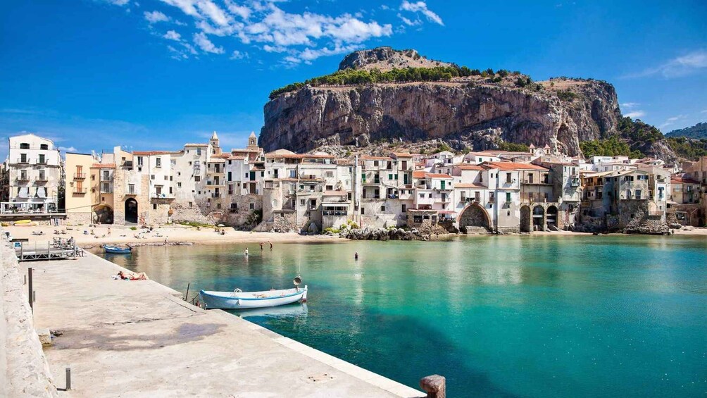 A coastal town with buildings along the waterfront, a clear blue sky, and a prominent cliff in the background. 3