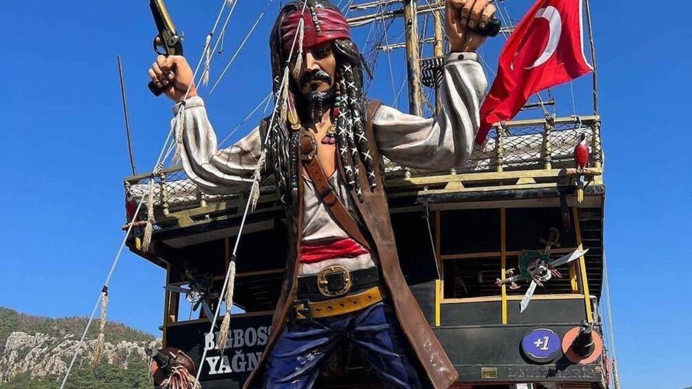 A pirate statue with a flag and a ship in the background. 1