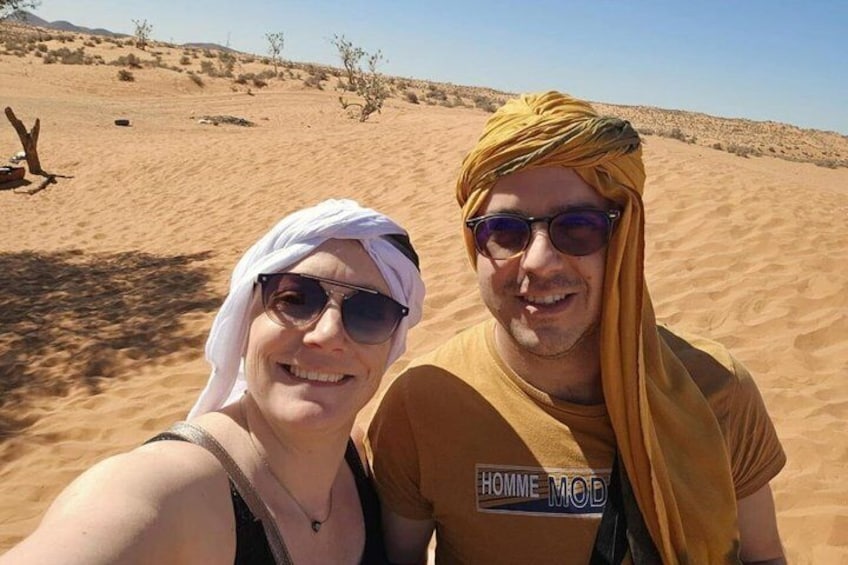 Two people in a desert landscape with sand dunes and sparse vegetation. 5
