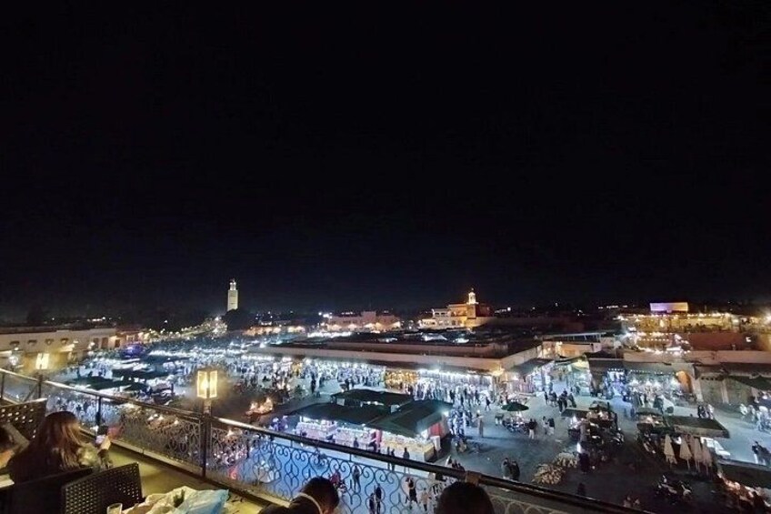 A nighttime view of a bustling market area with illuminated stalls and a prominent tower in the background. 5