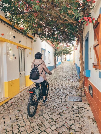 A person on a bicycle on a cobblestone street with buildings on either side. 3