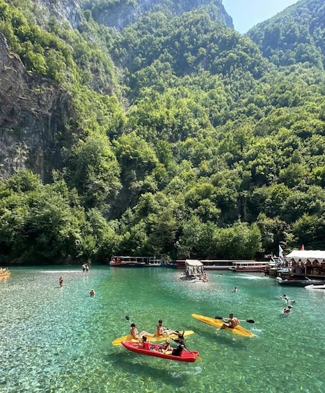A group of people kayaking on a clear river surrounded by lush green mountains. 1
