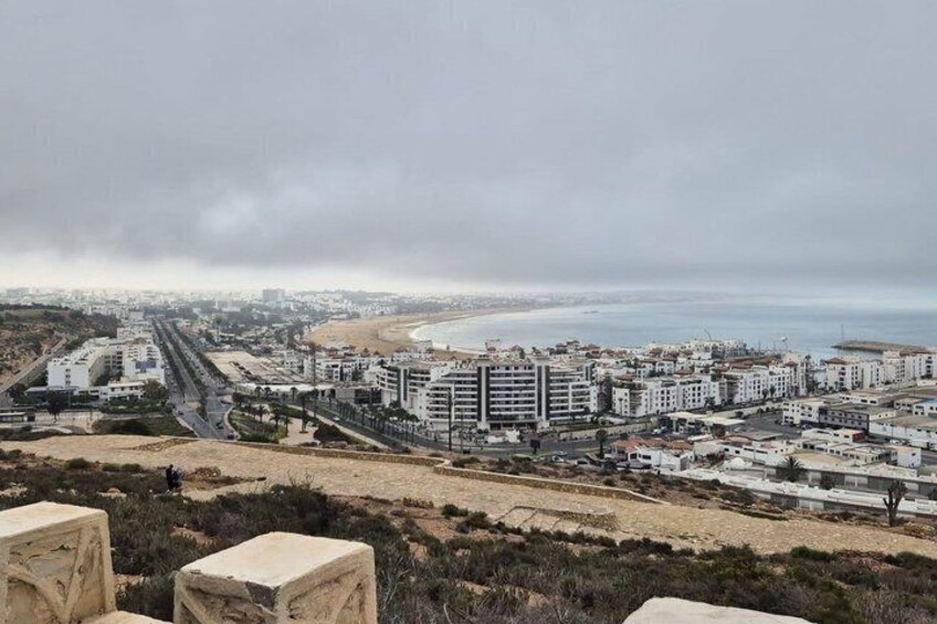 A coastal cityscape with buildings, a beach, and a road leading to the sea. 5