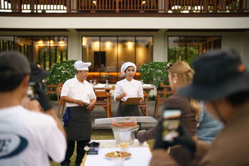 Chefs in white uniforms and striped aprons standing in front of a table with food. 2
