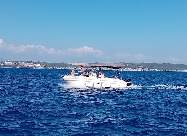 A white motorboat with passengers on a clear blue sea, with a coastline in the background. 5