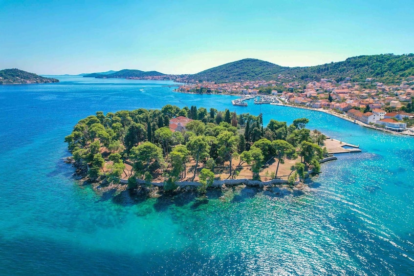 An aerial view of a coastal town with a prominent island featuring dense green trees and clear blue waters. 1