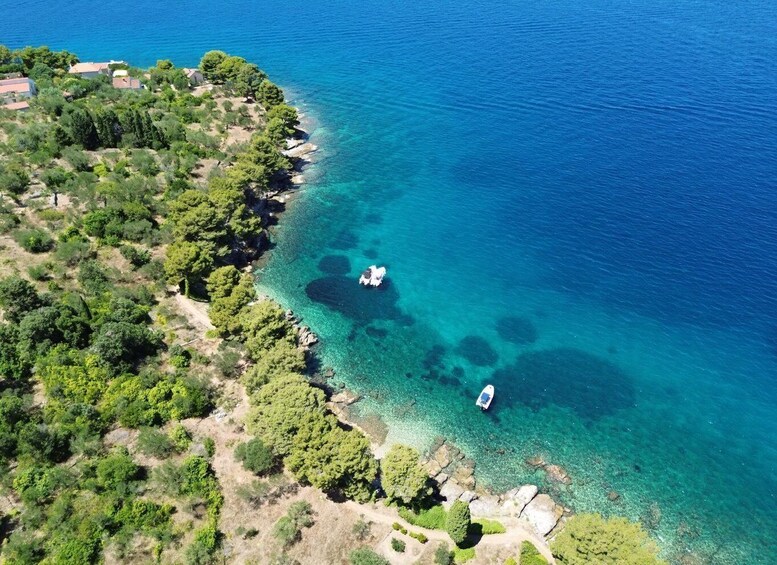 An aerial view of a coastal area with clear turquoise waters, rocky shoreline, dense greenery, and a small boat anchored near the shore. 2