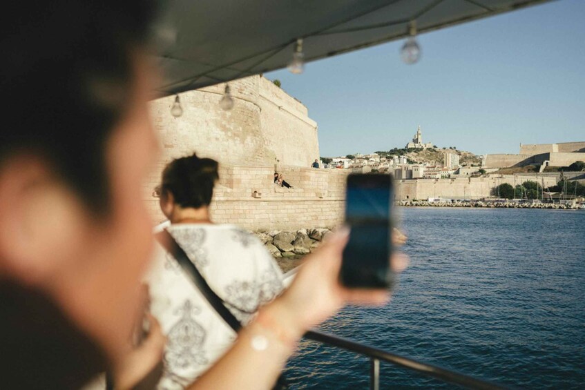 A person taking a photo of a coastal city with a prominent fort and a statue on a hill. 2