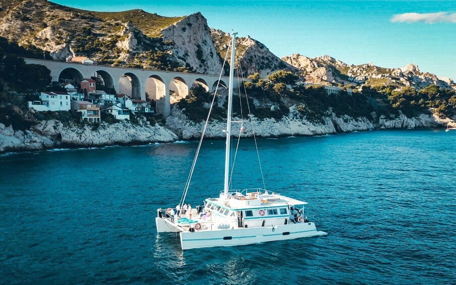 A sailboat on calm waters with a coastal town and a bridge in the background. 1