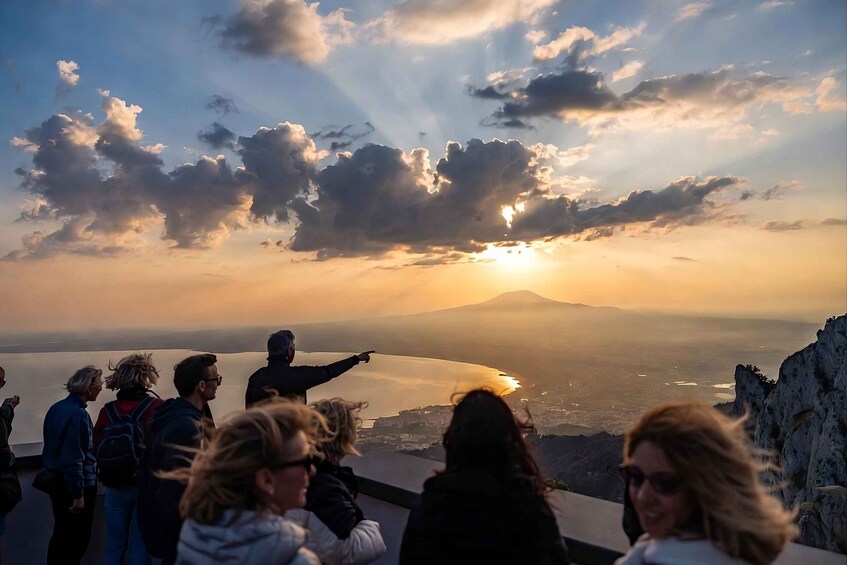 A group of people at a scenic overlook during sunset, overlooking a body of water and a distant mountain. 1