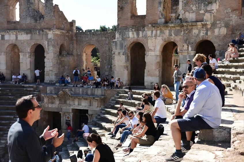 A historical stone structure with arches and ruins, surrounded by tourists. 2