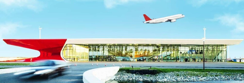 An airport terminal with a modern glass facade and a distinctive red and white sculpture in the foreground. 1
