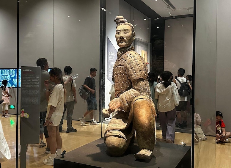 A large bronze statue of a seated warrior in a museum. 4