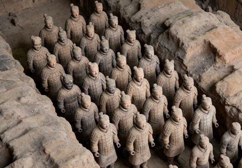 Terracotta soldiers arranged in rows, standing in a rocky enclosure. 2