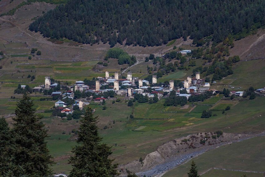 A village with medieval-style towers and houses nestled in a valley surrounded by forested hills. 5