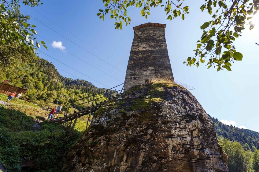 A stone tower on a hill with a wooden fence and people nearby. 3