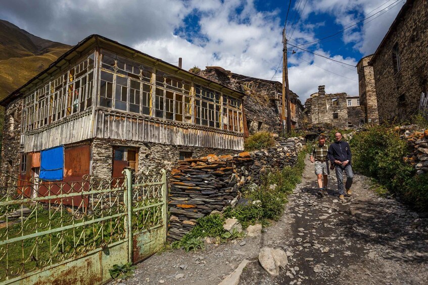 A rustic stone building with a wooden balcony, a stone wall, and a metal gate. 2