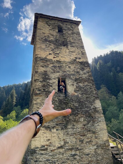 A person climbing a stone tower with a forested mountain backdrop. 1