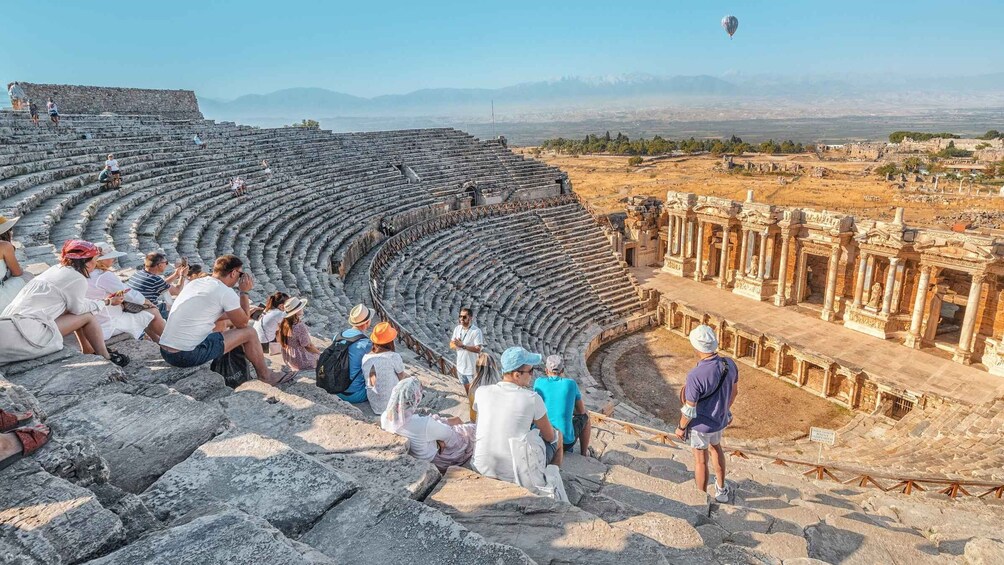 An ancient amphitheater with tourists sitting on the steps and standing around. 2