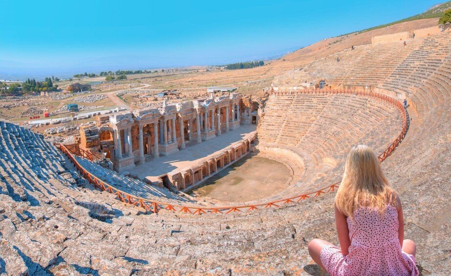 An ancient amphitheater with stone seating and columns, overlooking a hilly landscape. 3