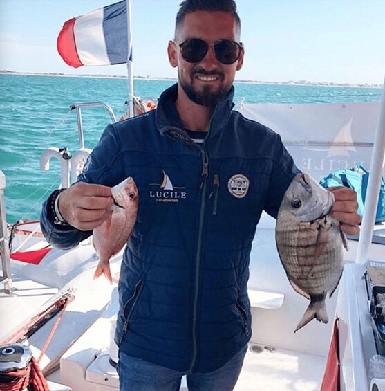 A person holding two fish on a boat with a clear blue sea in the background. 2