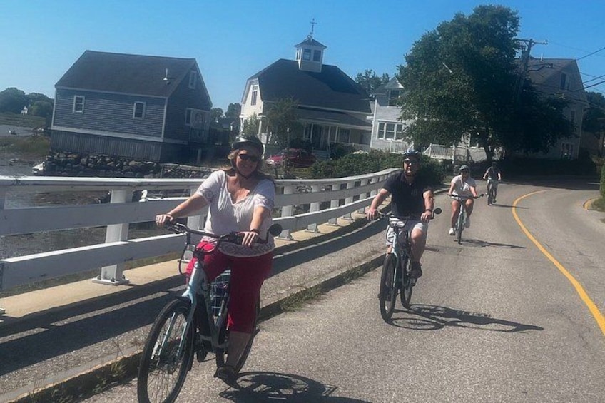 A paved path with cyclists, a white fence, and houses in the background. 5