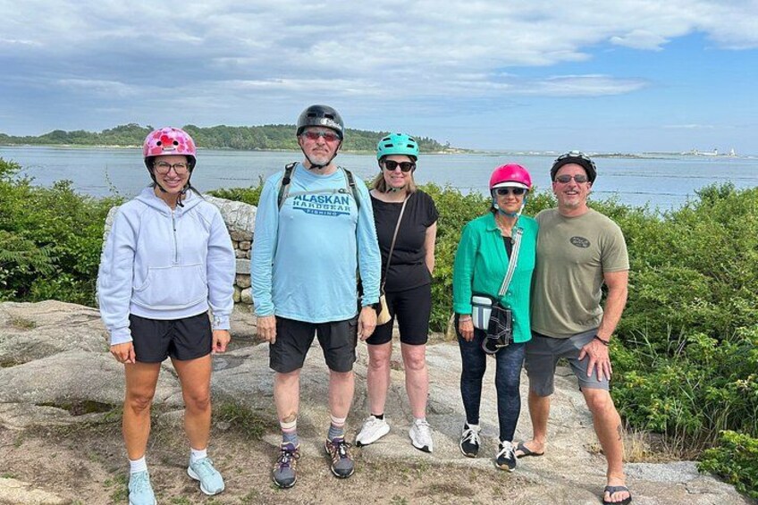 A group of people standing on a rocky shore with a body of water and greenery in the background. 3