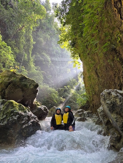 Two people in a river surrounded by rocks and greenery. 2