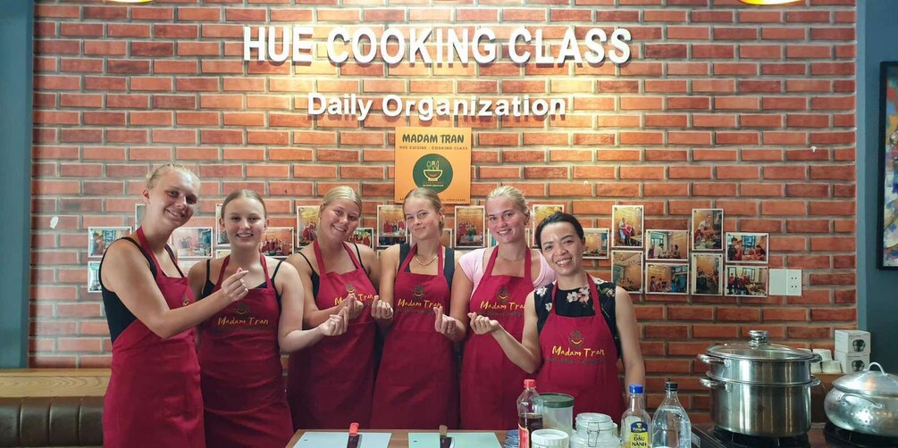A group of people in aprons standing in front of a brick wall with the text "HUE COOKING CLASS" and "Daily Organization". 5