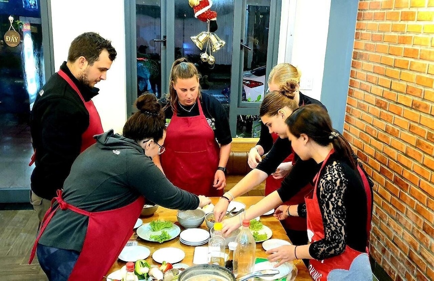 A group of people wearing aprons around a table with plates of food. 4