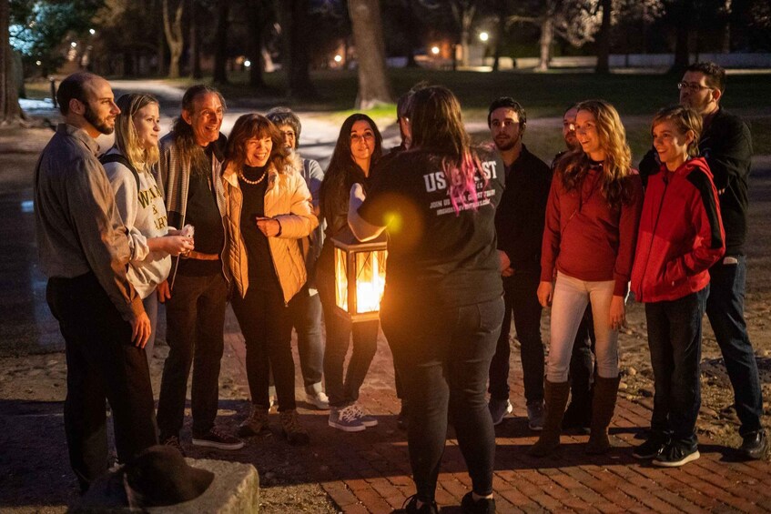 A group of people gathered around a person holding a lantern in a park at night. 2