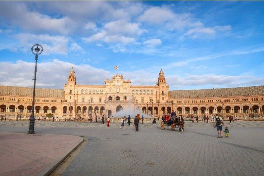 A large open plaza with a historic building featuring arches and columns, a fountain, and a horse-drawn carriage. 2