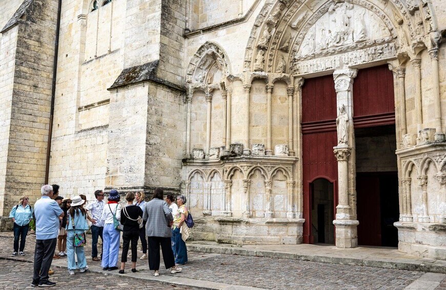 A group of people standing in front of a historic stone building with a red door and intricate carvings. 4