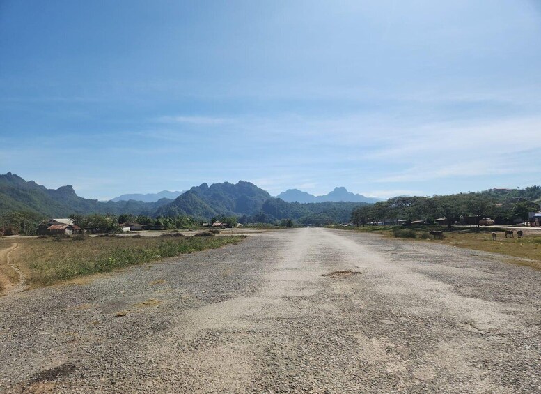 A gravel road leading through a rural area with scattered houses and mountains in the background. 3