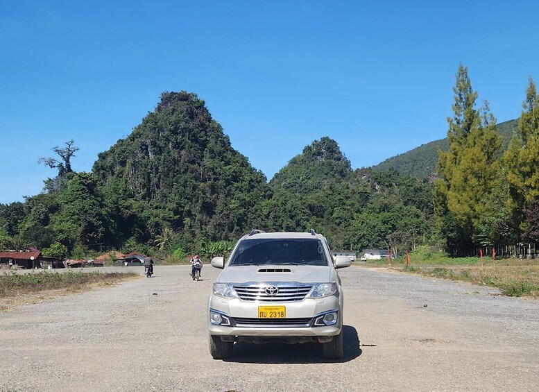 A silver car parked on a gravel road with a mountainous backdrop. 2