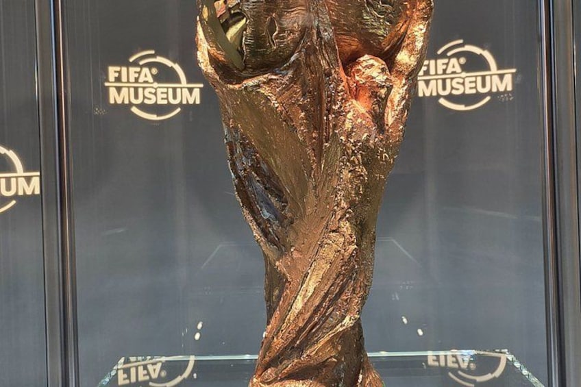 A golden trophy with a textured surface, set against a backdrop with the FIFA Museum logo. 3