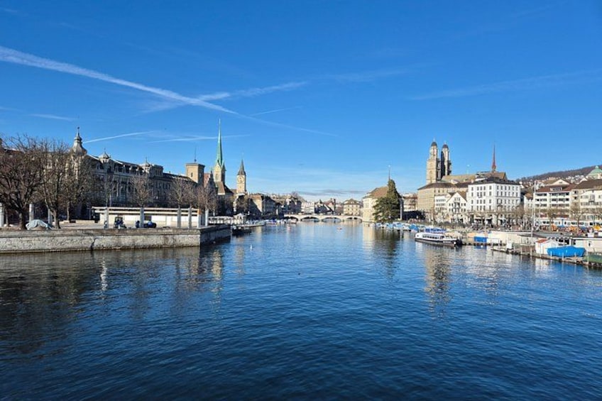 A river with boats, a bridge, and historic buildings including a church with a tall spire. 1
