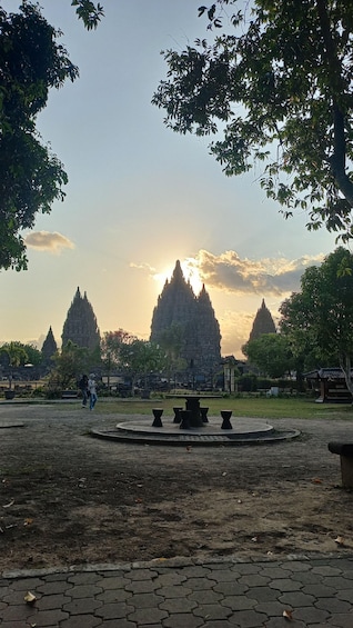A temple complex with multiple spires, surrounded by trees and a paved area with benches. 5