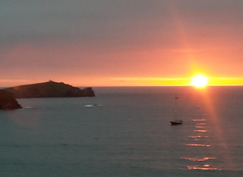 A sunset over a calm sea with a rocky coastline and a small boat. 2
