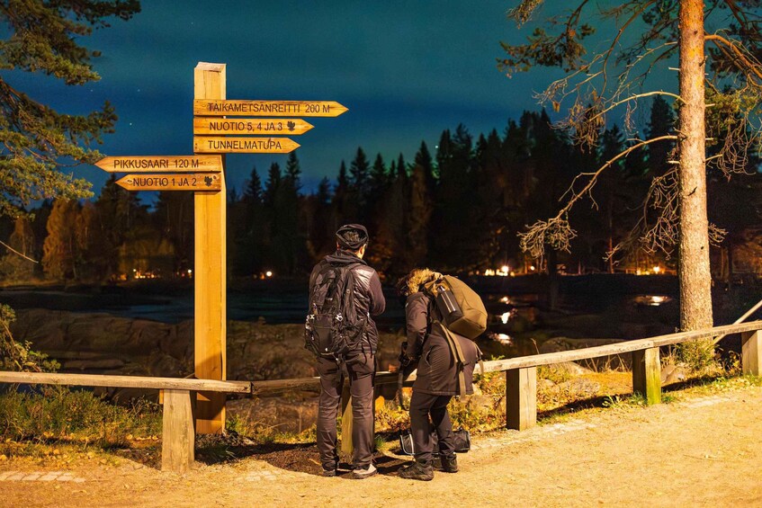 Two people standing by a wooden signpost with directional arrows pointing to various locations. 2