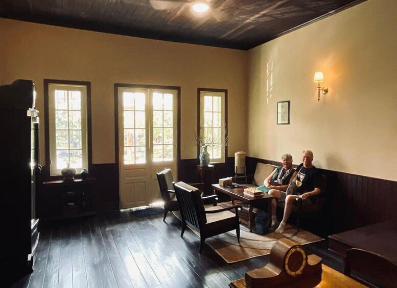 A cozy room with wooden floors, a sofa, a table, and three windows letting in natural light. 3
