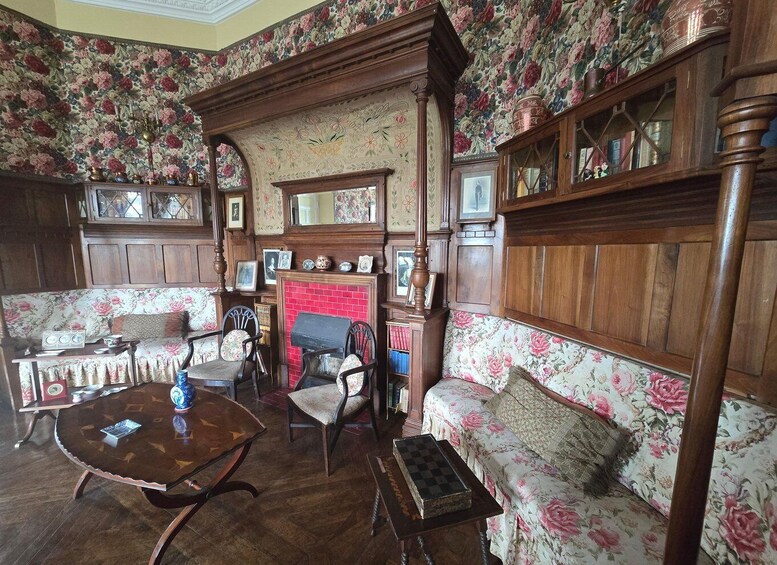 A vintage room with floral wallpaper, wooden furniture, and a fireplace. 4