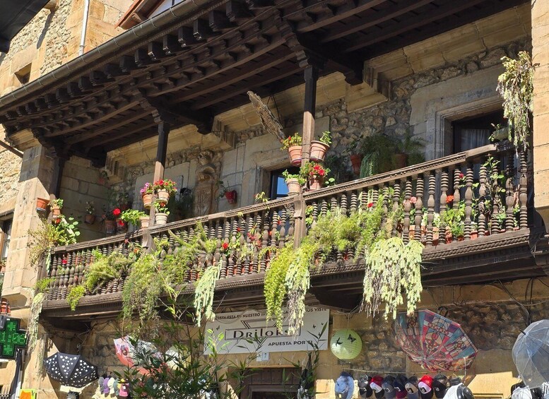 A traditional stone building with a balcony adorned with potted plants and a sign reading 'Drilos.' 2