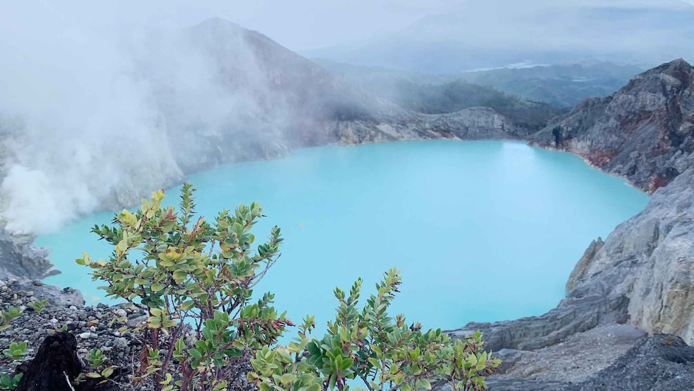 A volcanic crater with a turquoise lake surrounded by rocky terrain and sparse vegetation. 2