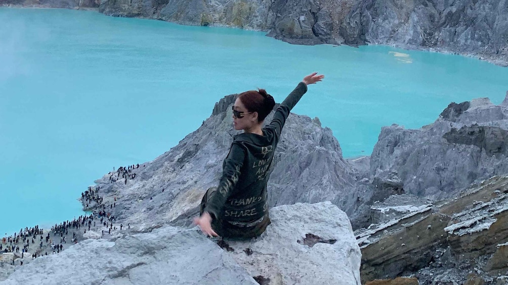 A person sitting on a rock with arms outstretched, overlooking a turquoise lake and a rocky mountain landscape. 4