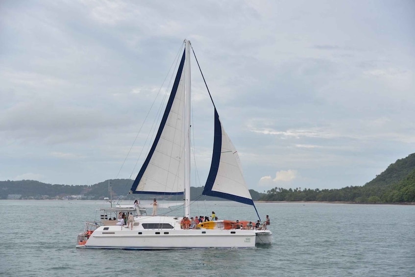 A sailboat with multiple passengers on a calm body of water, surrounded by a hilly landscape. 4