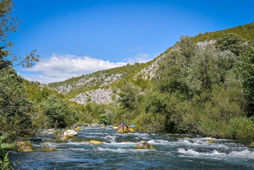 A kayaker navigating a river surrounded by lush greenery and rocky hills. 3