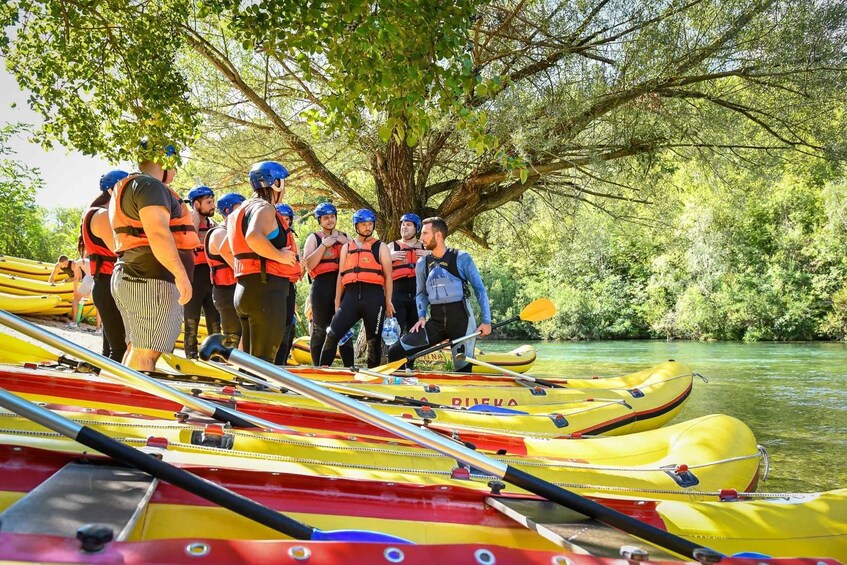 A group of people in life jackets and helmets gathered around yellow kayaks by a river. 4