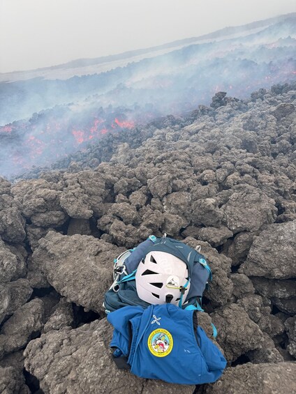 A person with a helmet and backpack on a rocky terrain with visible lava flows in the background. 3
