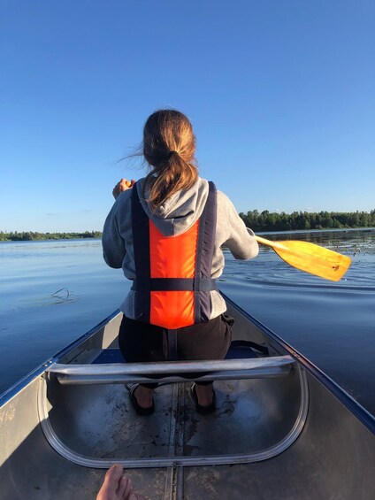 A person in a canoe wearing a life jacket, paddling on a calm body of water. 3